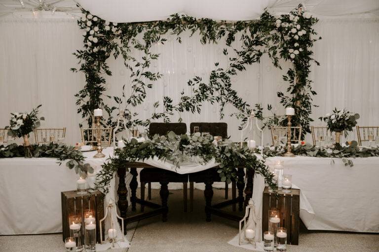 Natural birch wood wedding sweetheart table backdrop with lush greenery and white floral accents by ILLUME at Linden Hall in Dawson, PA.